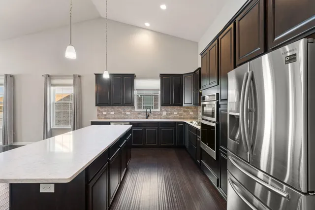 a large kitchen with a large counter top a sink stainless steel appliances and cabinets