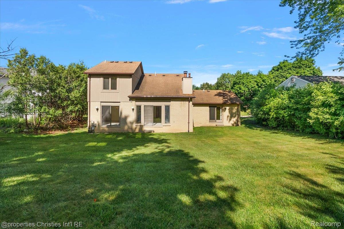 37224 Chesapeake Road Farmington, MI 48335 - Photo 10 of 50 Expansive green lawn with a two-story beige exterior featuring multiple windows and sliding glass doors