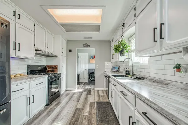 a kitchen with stainless steel appliances granite countertop a stove a white cabinet and a granite countertops with wooden floor