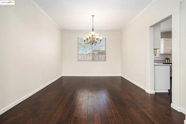 an empty room with wooden floor chandelier and windows