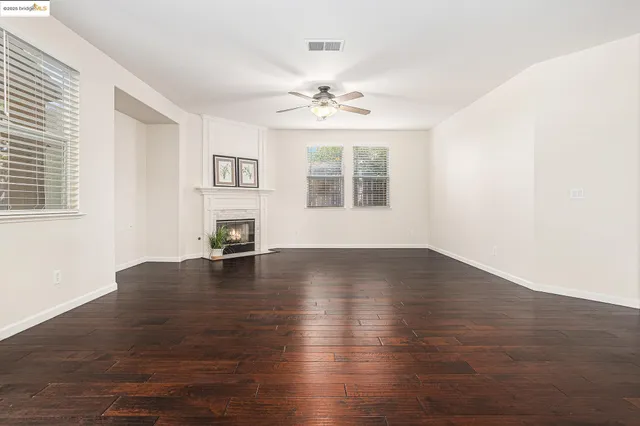 an empty room with wooden floor chandelier fan and windows
