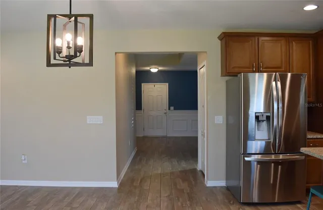 an empty room with wooden floor kitchen view and windows