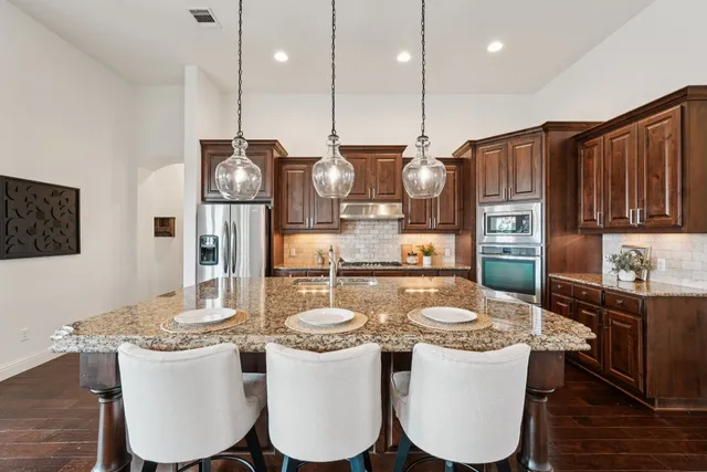 a dining room with stainless steel appliances kitchen island granite countertop a table chairs and a refrigerator