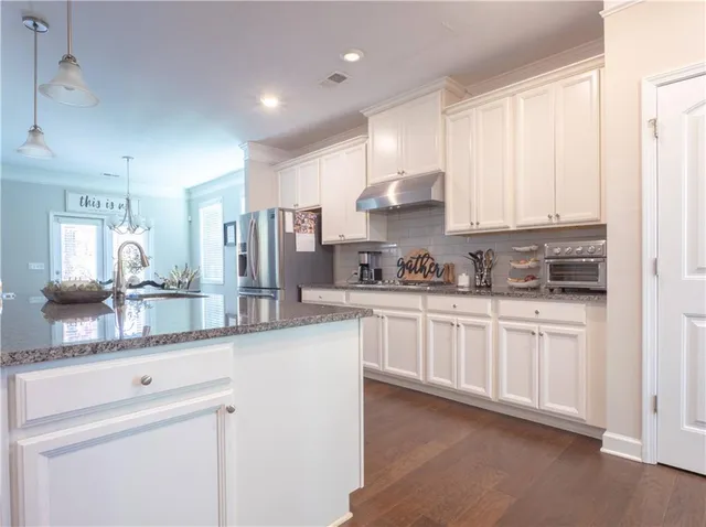 a kitchen with stainless steel appliances granite countertop a refrigerator a sink and white cabinets