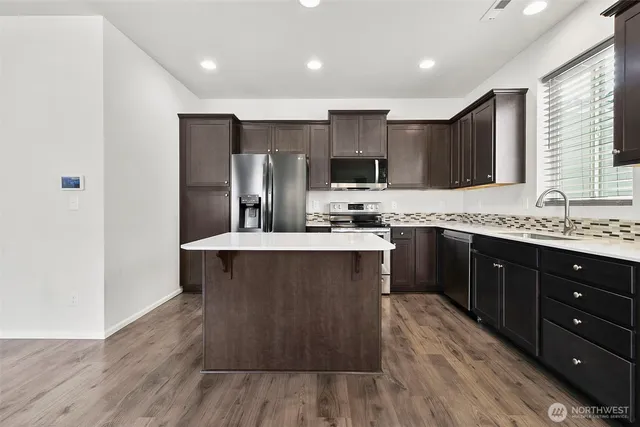 a kitchen with kitchen island granite countertop wooden floors stainless steel appliances a sink and a window