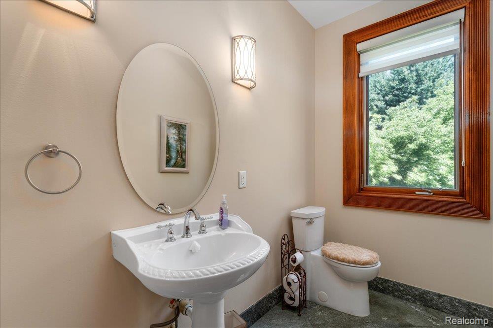 3543 Cedar Brook Drive Rochester, MI 48309 - Photo 66 of 99 Pedestal sink with polished chrome fixtures, oval mirror, wall sconce lighting, and a window with wood trim