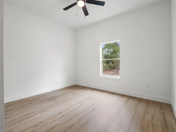 an empty room with wooden floor chandelier fan and windows