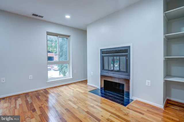 a view of an empty room with wooden floor fireplace and a window
