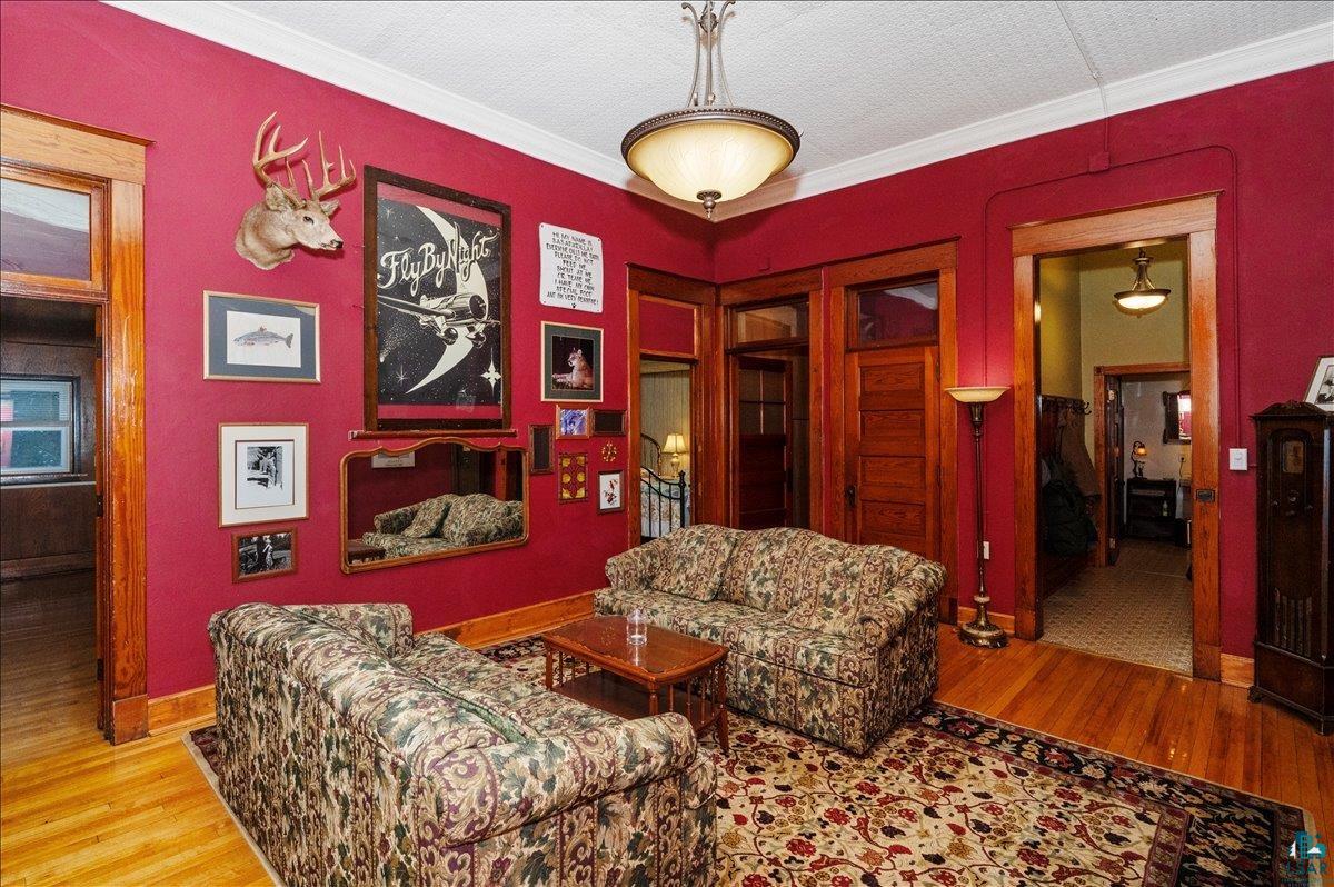 7596 Werner Road Virginia, MN 55792 - Photo 11 of 27 Living area featuring hardwood flooring, red wall paint, white crown molding, and wooden door frames