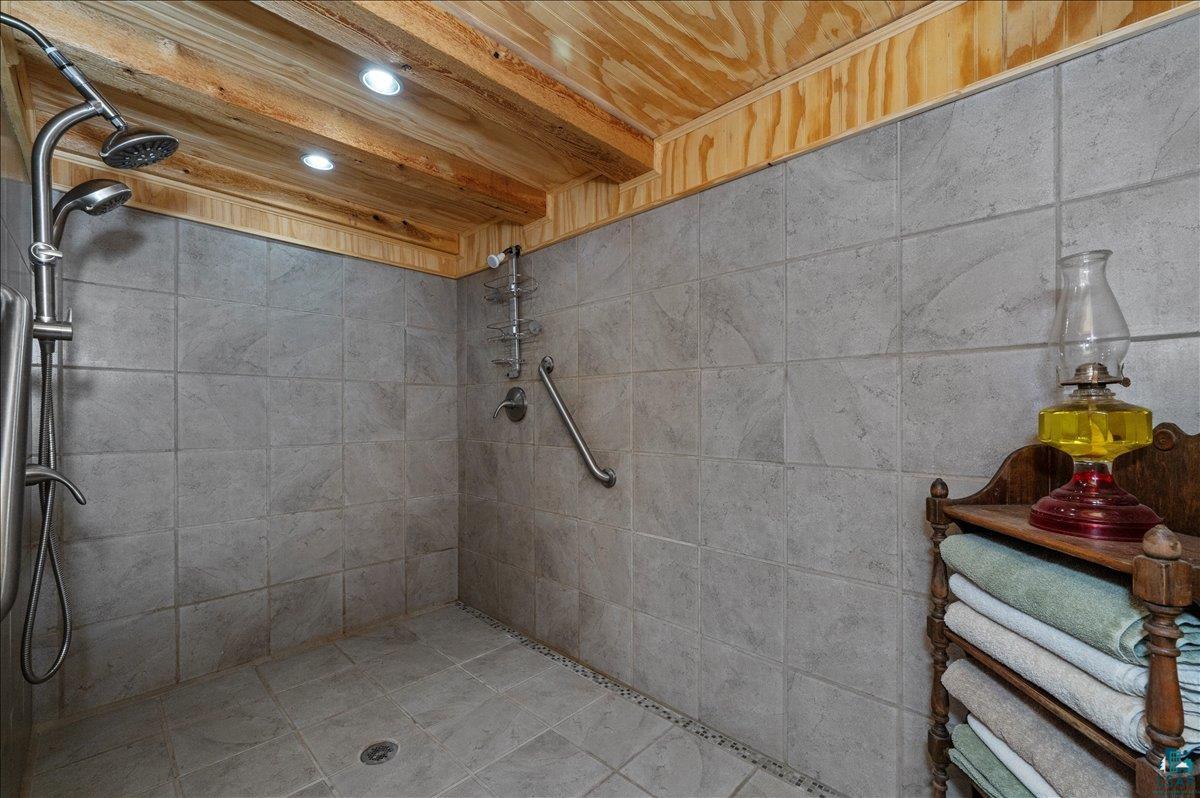 7596 Werner Road Virginia, MN 55792 - Photo 14 of 27 Walk-in shower with gray tile walls and floor, featuring a dual shower head system and recessed ceiling lighting