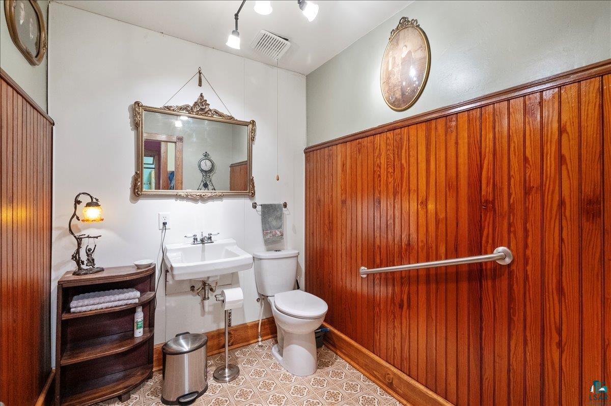 7596 Werner Road Virginia, MN 55792 - Photo 17 of 27 Bathroom featuring rich wood paneling, a classic pedestal sink, decorative wall mirror, patterned tile flooring, and integrated wall lighting
