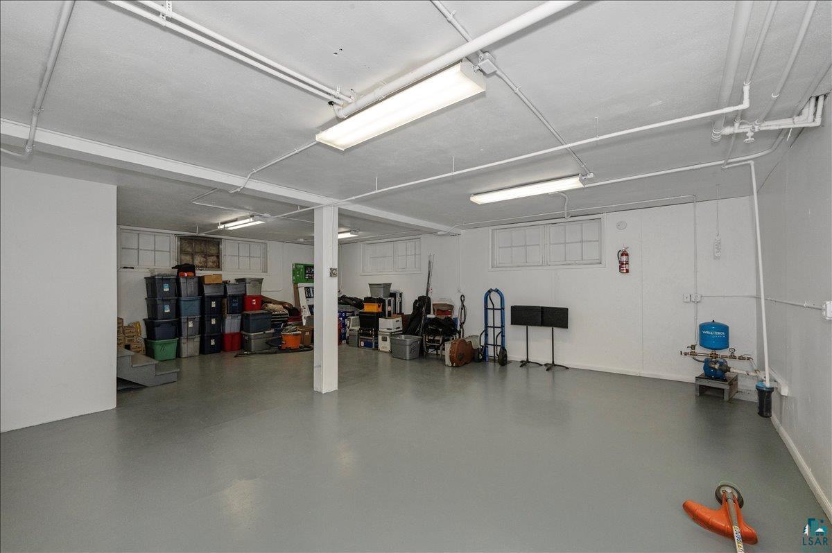 7596 Werner Road Virginia, MN 55792 - Photo 20 of 27 Spacious utility room featuring a painted concrete floor, white walls, exposed ceiling pipes, and fluorescent lighting fixtures