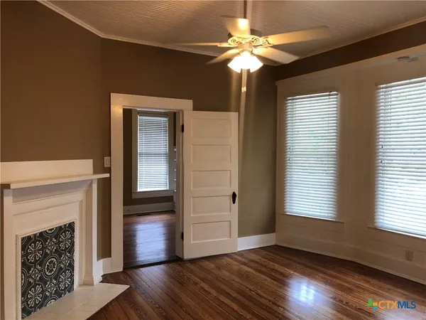a view of an empty room with wooden floor fireplace and a window