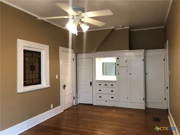 a view of an empty room with wooden floor and fan