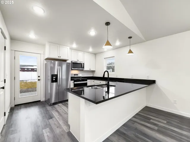 a kitchen with stainless steel appliances granite countertop a refrigerator a sink dishwasher a stove and white countertops with wooden floor