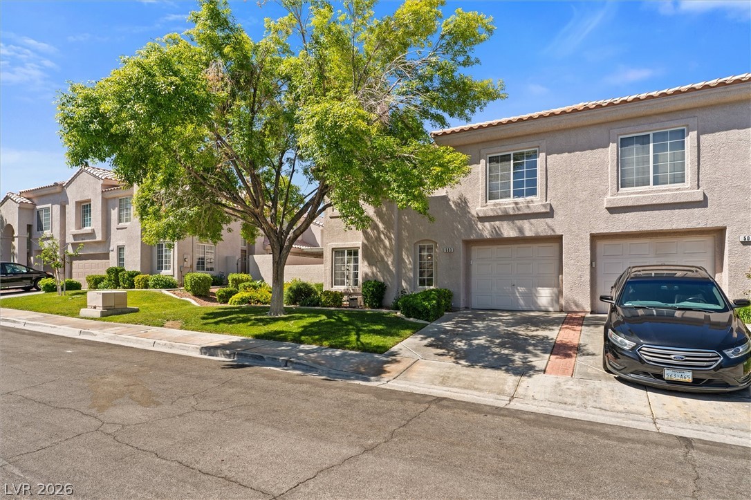 503 Rafkin Place Henderson, NV 89052 - Photo 2 of 18 A welcoming facade showcases stucco construction and integrated garages, framed by mature trees and verdant landscaping.