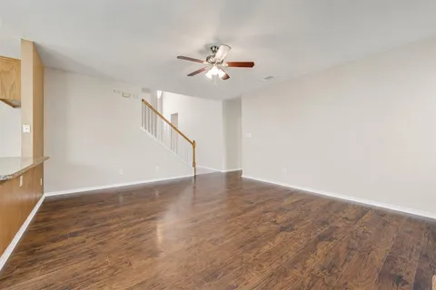 a view of an empty room with wooden floor and a ceiling fan