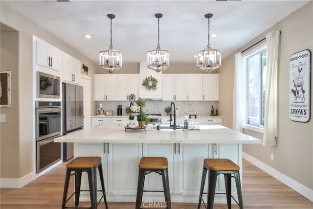 a kitchen with stainless steel appliances kitchen island granite countertop a refrigerator a stove a sink dishwasher and white cabinets with wooden floor