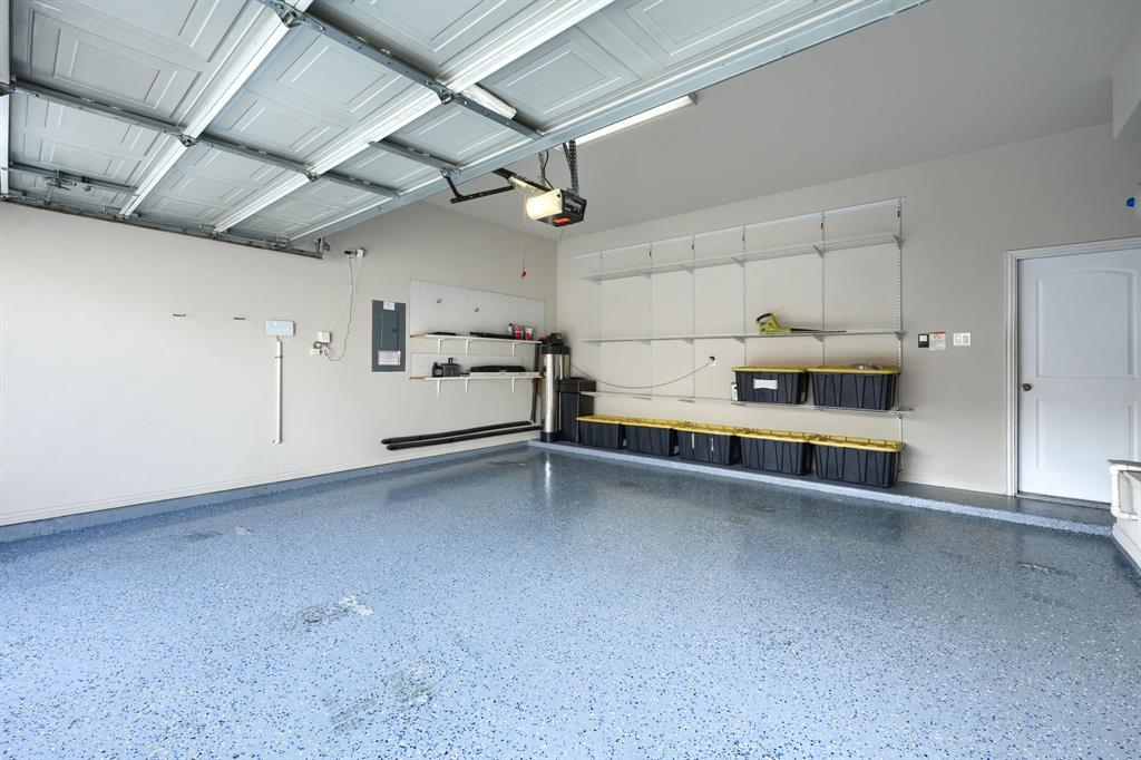2246 Longview Road Irving, TX 75063 - Photo 39 of 40 Garage featuring a light blue speckled epoxy floor, white paneled garage door, built-in wall shelving, a side access door, and recessed lighting