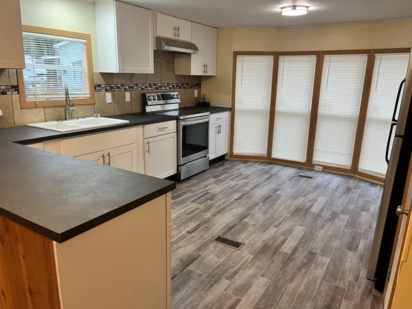 a kitchen with stainless steel appliances granite countertop a refrigerator a sink dishwasher a stove top oven a refrigerator and white cabinets with wooden floor