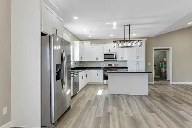 a kitchen with kitchen island granite countertop a refrigerator oven a sink dishwasher and white cabinets with wooden floor