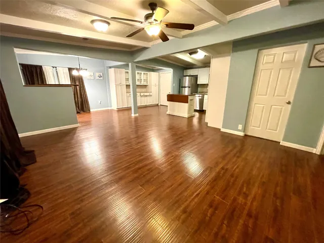 a view of an empty room with wooden floor and a kitchen