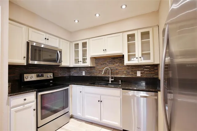 a kitchen with stainless steel appliances granite countertop a refrigerator a sink and white cabinets