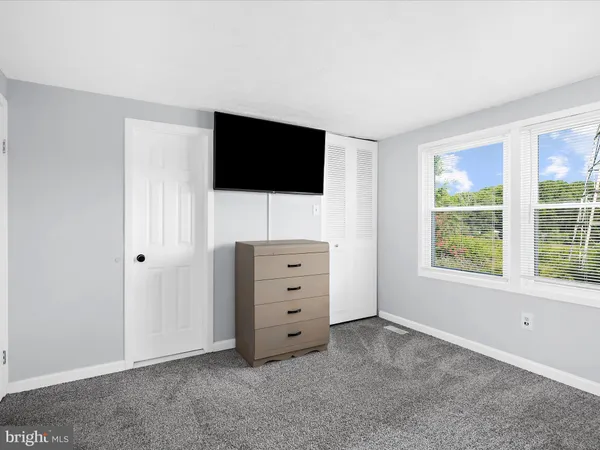 a room with a flat screen tv on dresser and a window