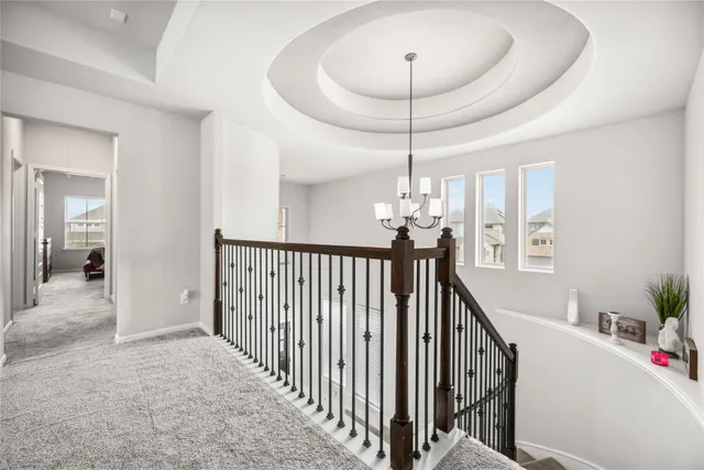 a view of a hallway to a livingroom with wooden floor stairs and a chandelier