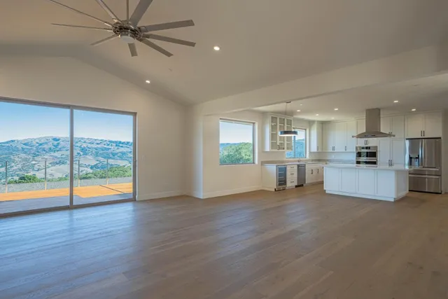 a view of an empty room with wooden floor and a kitchen