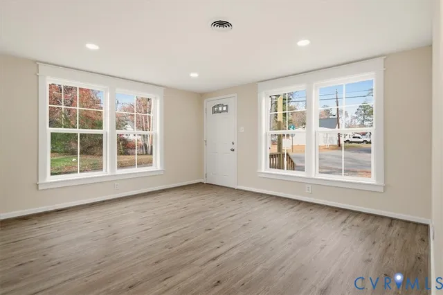 a view of an empty room with wooden floor and windows