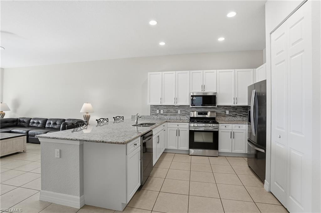 4194 Amelia Way Naples, FL 34119 - Photo 11 of 44 a kitchen with stainless steel appliances granite countertop a stove top oven a sink dishwasher and a refrigerator with wooden cabinets