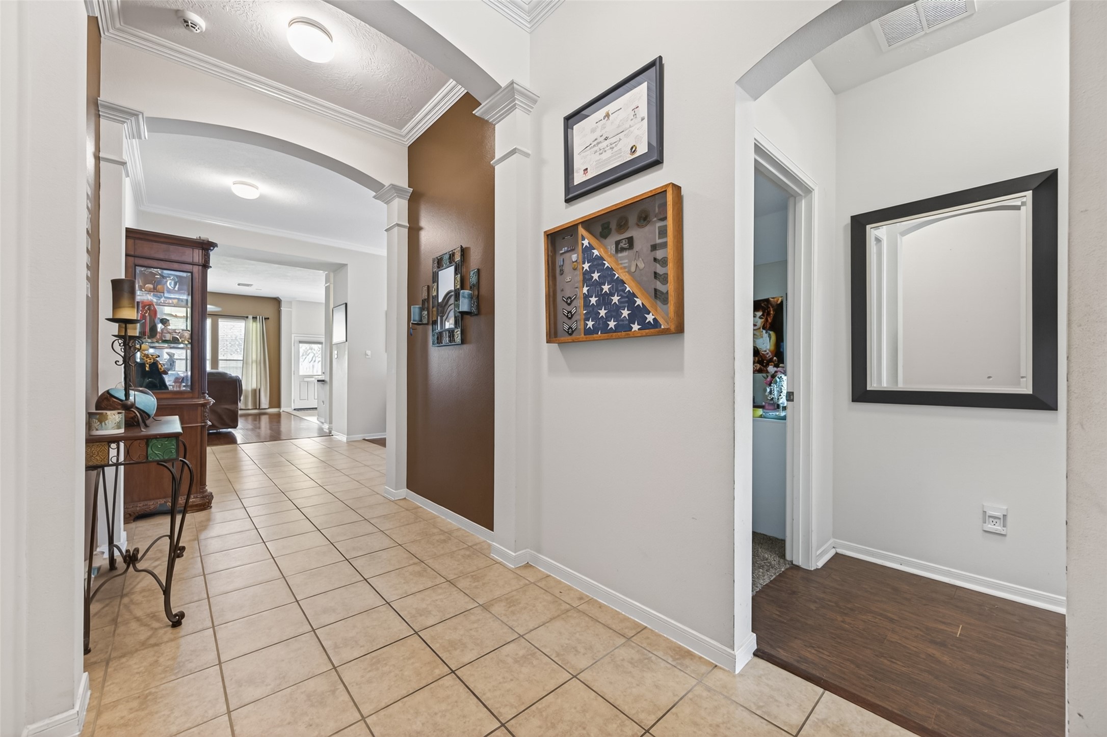 8622 Henrico Lane Rosenberg, TX 77469 - Photo 7 of 20 This photo showcases a welcoming hallway with tile flooring, arched entryways, and decorative wall accents. The space leads into a bright living area with visible natural light, offering a warm and inviting atmosphere.