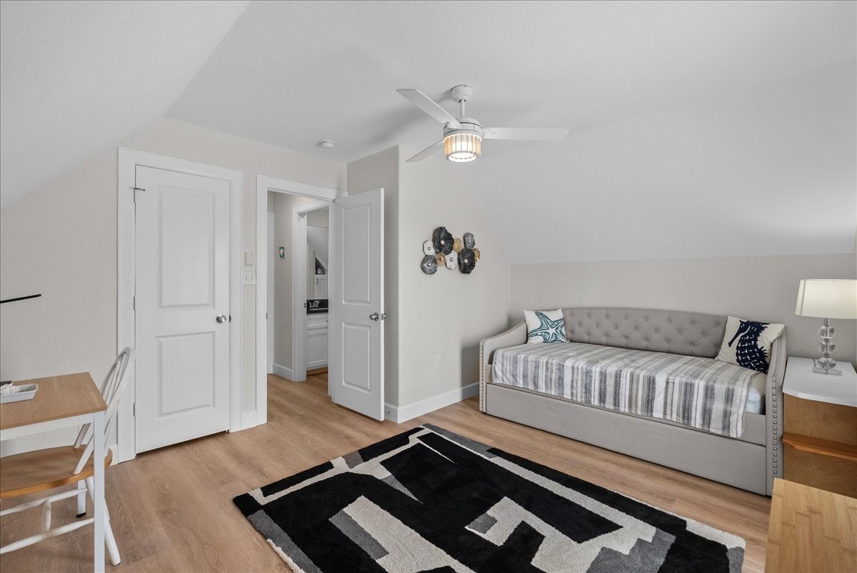 130 Beachcomber Avenue Surfside Beach, TX 77541 - Photo 22 of 33 This cozy bedroom features a stylish daybed, wooden flooring, and a modern ceiling fan. It includes a small workspace with a desk and chair, and offers a view into an adjacent bathroom. The decor is neutral with a touch of modern flair.