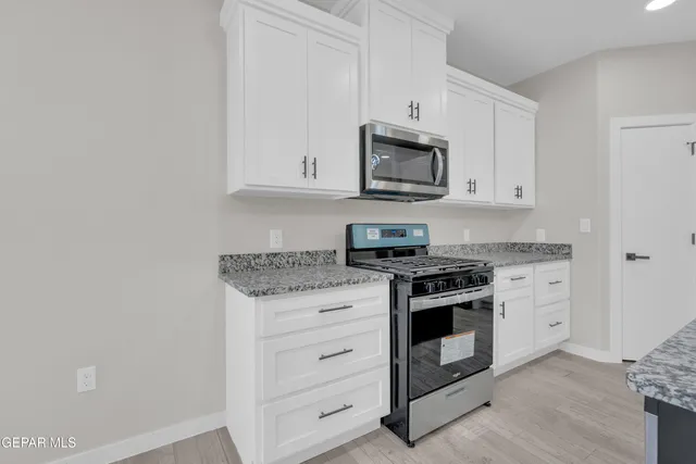 a kitchen with stainless steel appliances granite countertop white cabinets a stove a microwave and a sink
