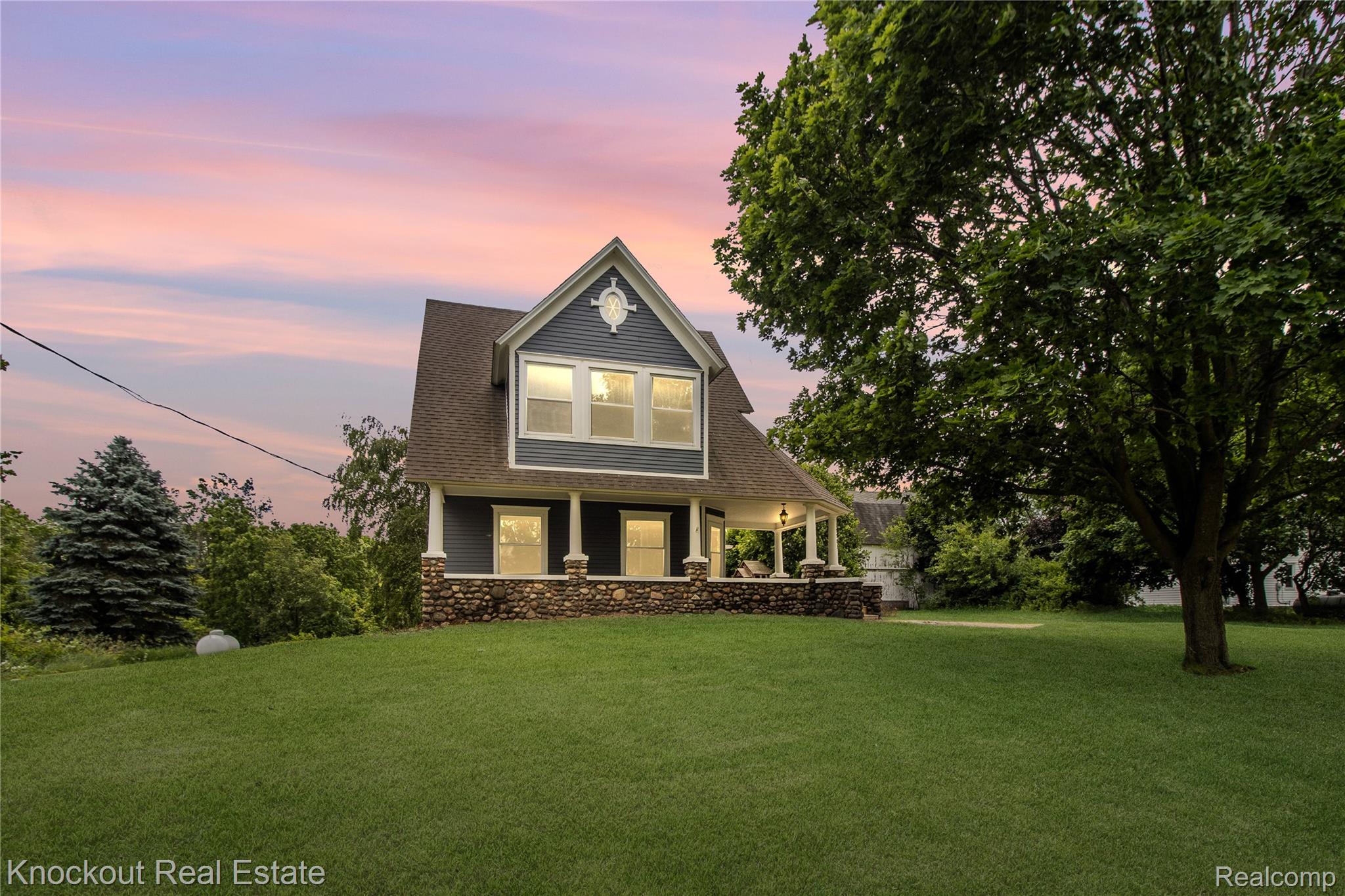 19983 West Ridge Road Henderson, MI 48841 - Photo 2 of 76 Two-story residence featuring a covered front porch with stone pillars, grey siding, white trim details, and a dark shingled roof