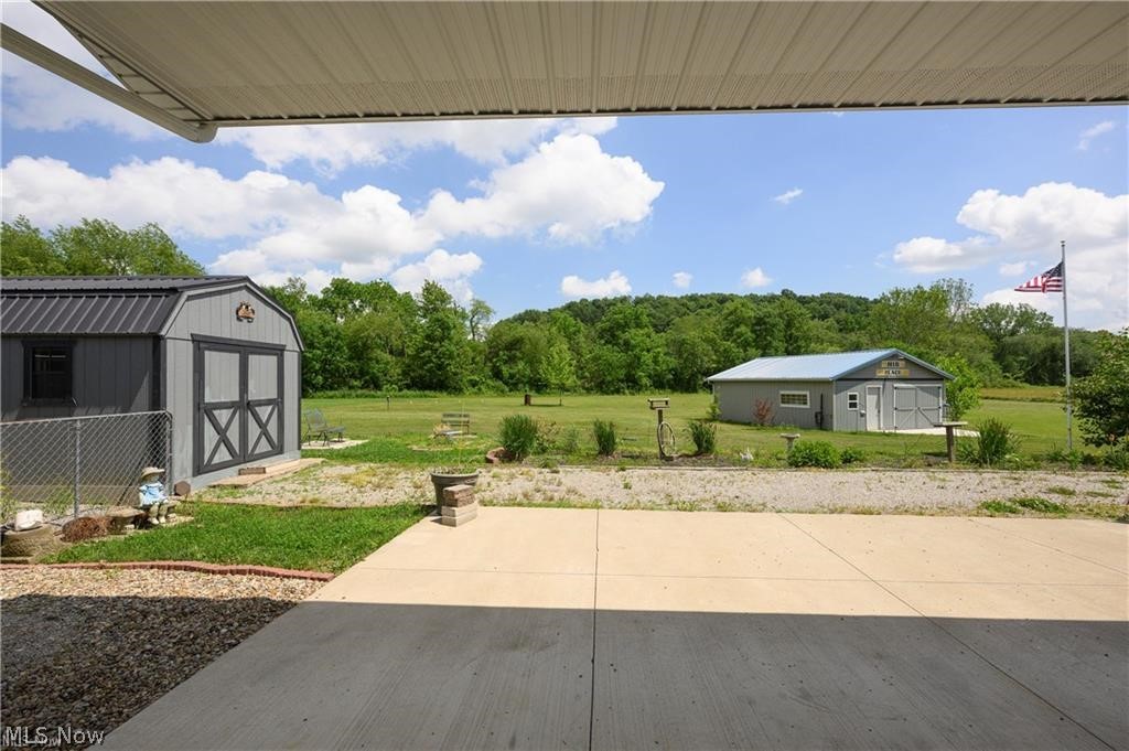 9427 Stonecreek Road Southwest Newcomerstown, OH 43832 - Photo 5 of 26 Expansive concrete patio with a covered awning, two detached storage buildings, and a large open field