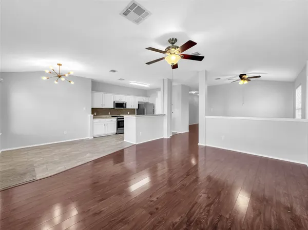 a view of an empty room and kitchen with wooden floor