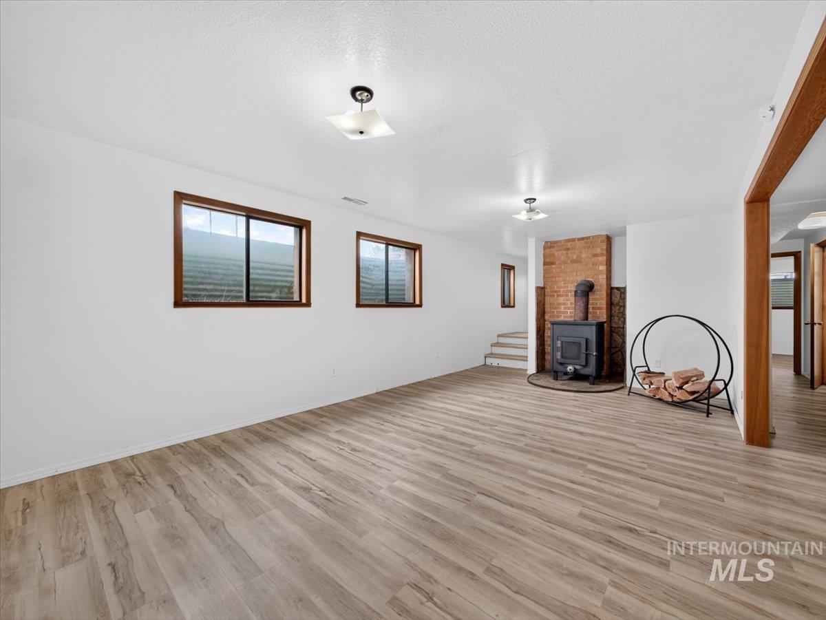 8989 Hillview Road Emmett, ID 83617 - Photo 33 of 50 Spacious room featuring wood-finish flooring, a brick accent wall, and an exposed stovepipe leading to a cast iron wood stove