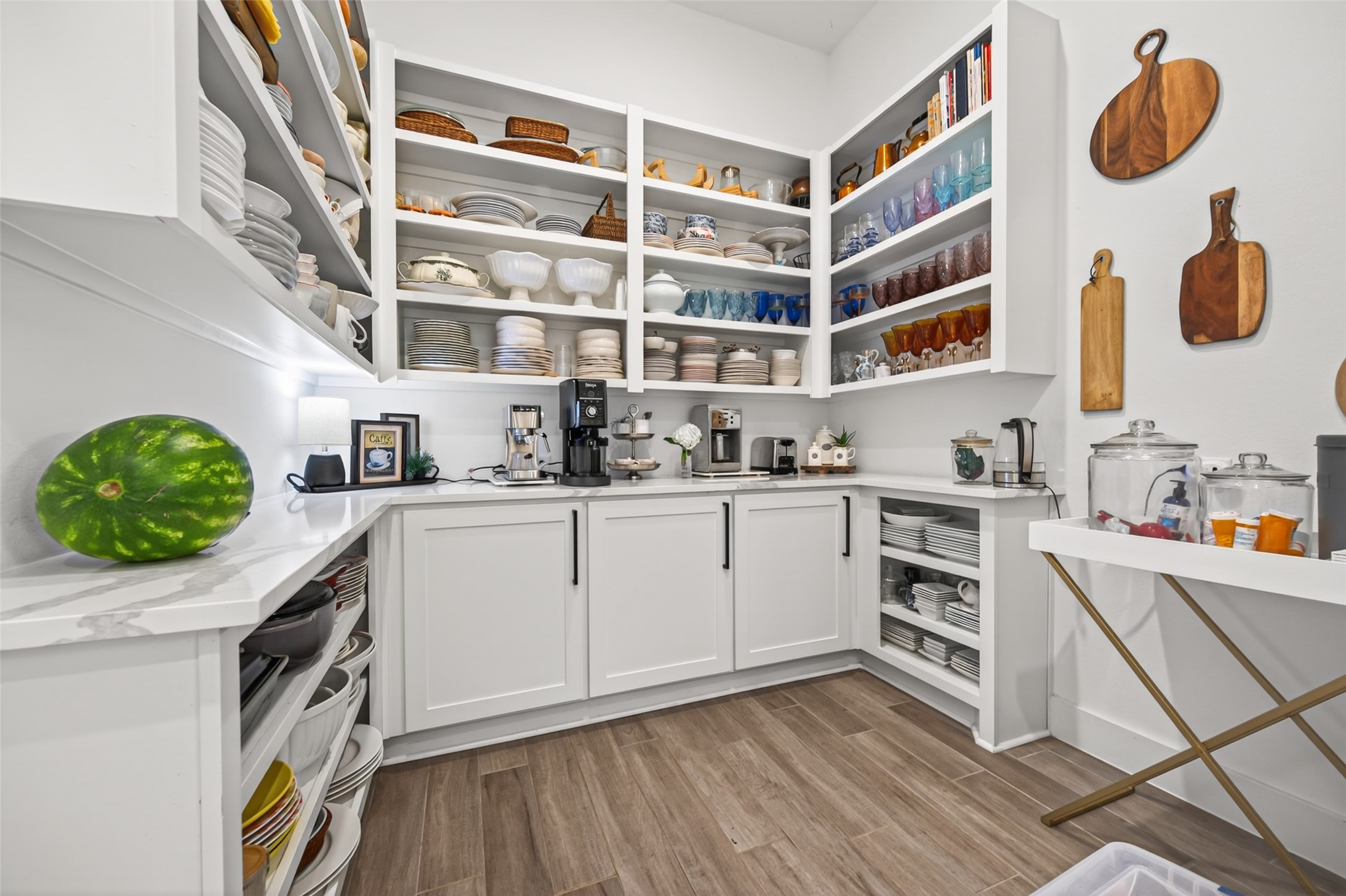 29612 Fulshear Lake Trace Fulshear, TX 77406 - Photo 25 of 48 This pantry features open shelving with neatly organized dishes and glassware, ample countertop space, and modern cabinetry. The wooden floor adds warmth, while decorative cutting boards provide a stylish touch. Perfect for extra kitchen storage and organization.