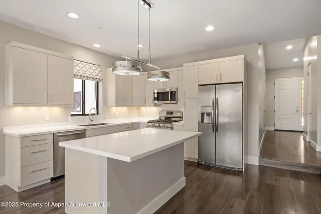 a large kitchen with a center island wooden floor and stainless steel appliances