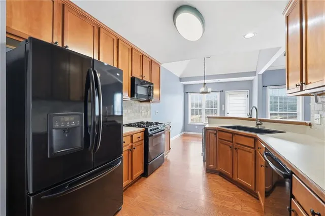 a kitchen with stainless steel appliances granite countertop a refrigerator a sink dishwasher a stove and white countertops with wooden floor