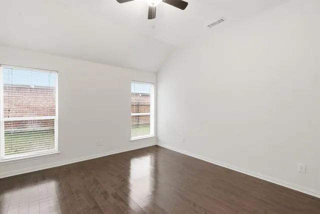 an empty room with wooden floor fan and windows