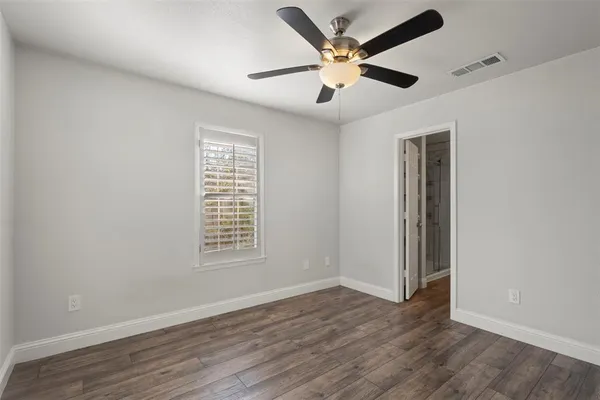 an empty room with wooden floor ceiling fan and windows