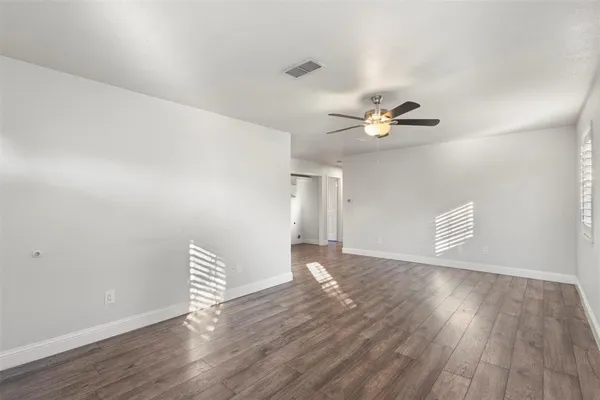a view of an empty room with wooden floor and a ceiling fan