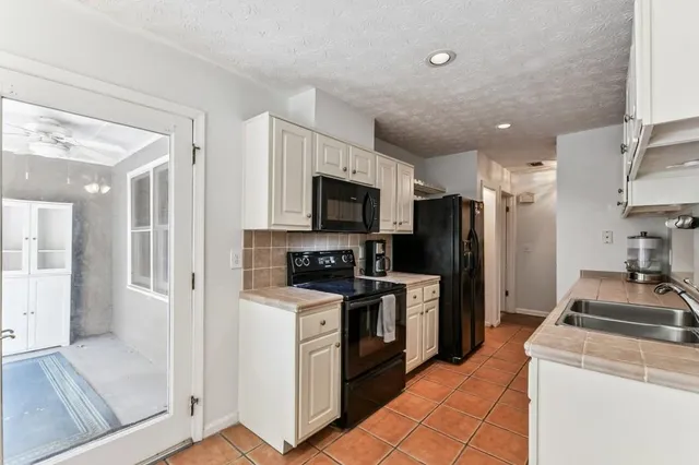 a kitchen with granite countertop a refrigerator a sink a stove top oven and cabinets