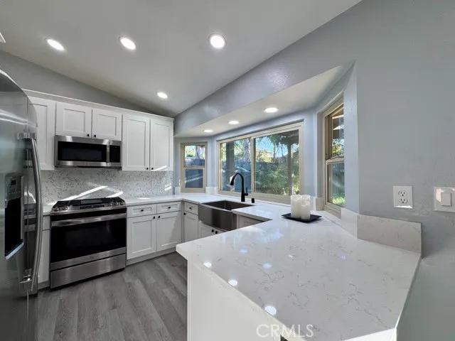 a open kitchen with stainless steel appliances granite countertop a stove top oven a sink dishwasher a dining table and chairs with wooden floor