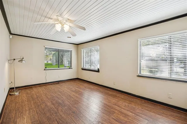 an empty room with wooden floor chandelier fan and windows