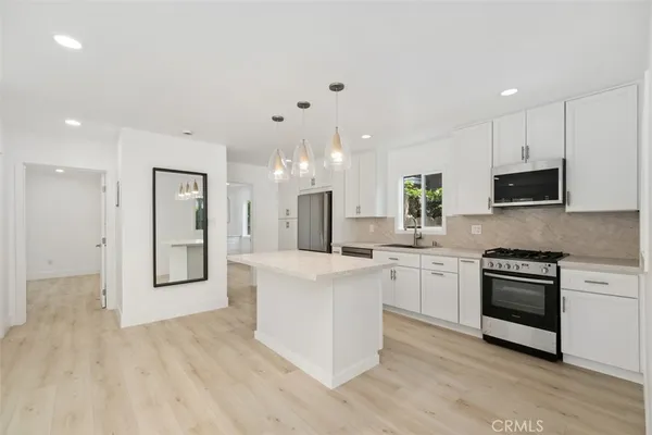a kitchen with stainless steel appliances granite countertop a stove top oven a sink dishwasher and a refrigerator with wooden floor