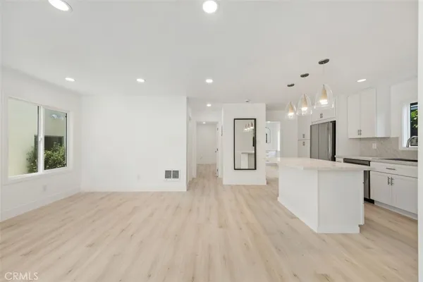 a large white kitchen with kitchen island a sink dishwasher a refrigerator and white cabinets with wooden floor